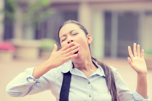 Sleepy young business woman covering with hand opened mouth yawning