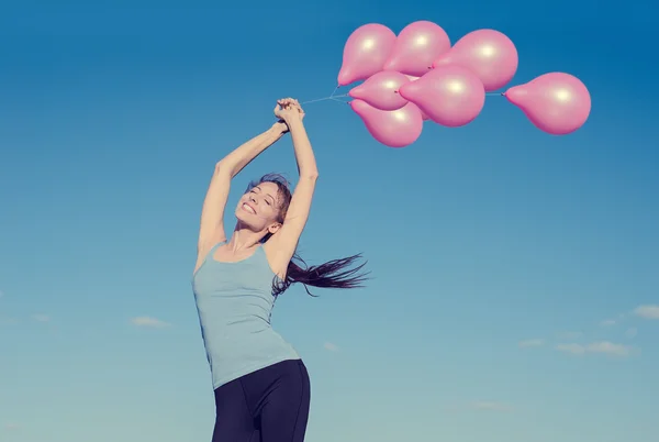 Woman with arms raised holding pink flying balloons