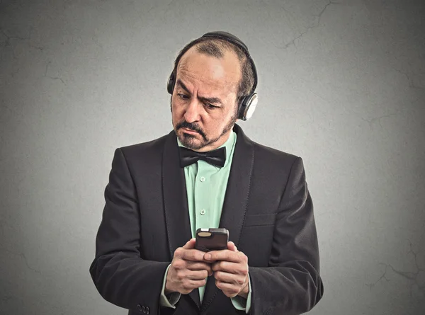 Confused man listening music with pair of headphones looking at his smartphone
