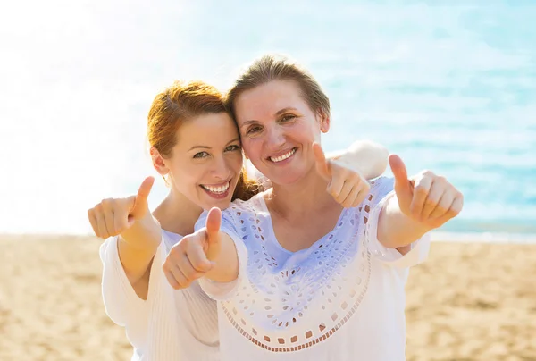 Joyful women mother daughter showing thumbs up having fun vacation on beach
