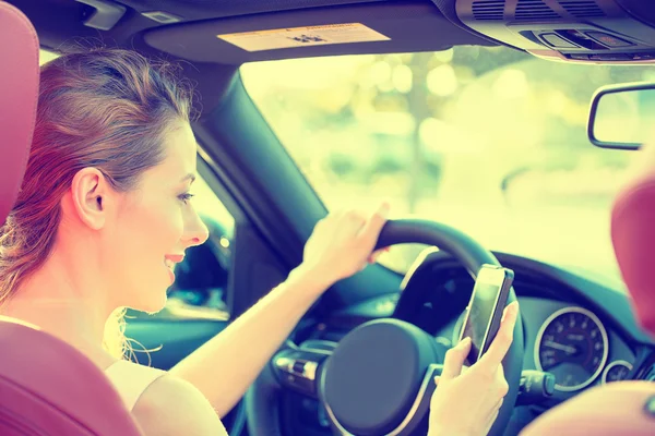 Businesswoman sending text message using mobile phone while driving car