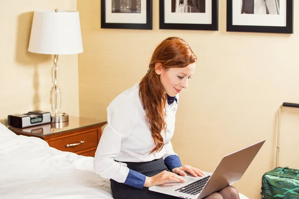 Businesswoman working on laptop sitting on the bed in hotel room