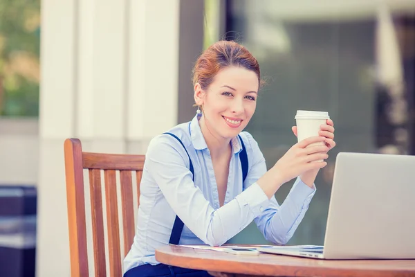 Woman drinking coffee working on computer laptop outside corporate office