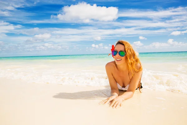 Woman with sunglasses laying on beach covered in ocean waves