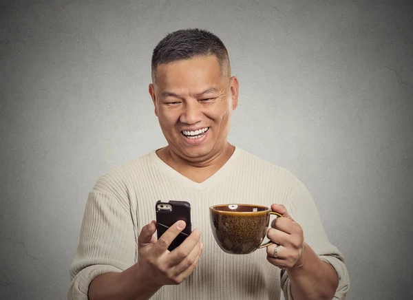 Happy middle aged man reading good news on smartphone drinking cup coffee
