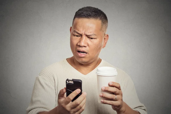 Worried man reading bad news on smart phone drinking cup of coffee