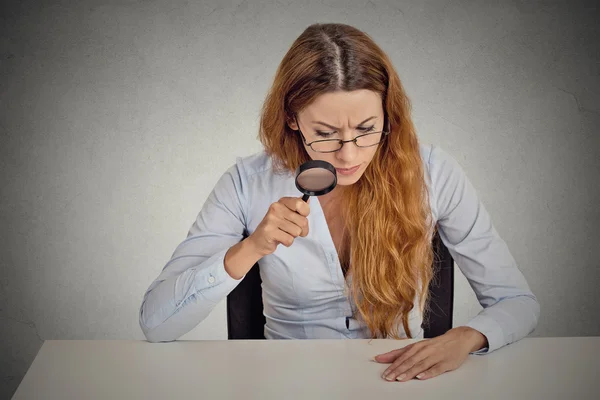 Business woman with glasses skeptically looking through magnifying glass at table