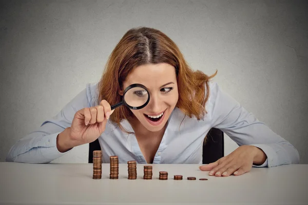 Greedy business woman looking at stack of coins through magnifying glass