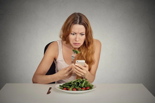 Displeased girl eating green salad looking at phone seeing bad news