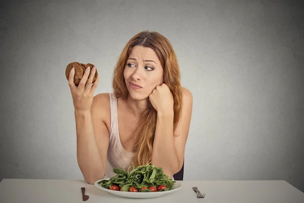 Woman deciding whether to eat healthy food or sweet cookies