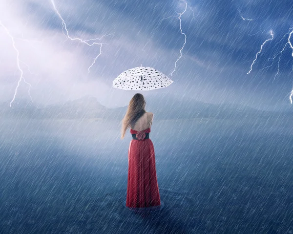 Woman in red dress under umbrella on countryside flooded field
