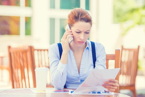 Unhappy, serious woman talking on phone holding looking at documents