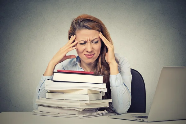 Stressed woman sitting at desk with books computer