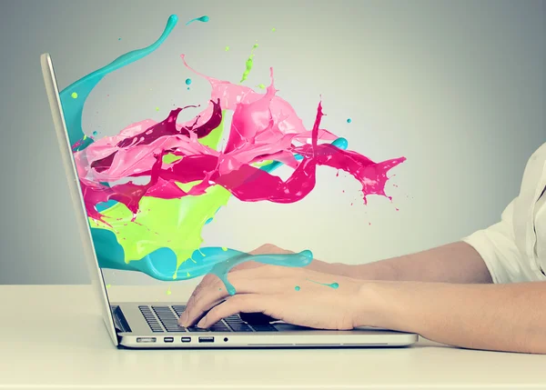 Hands on keyboard with colorful splashes out of monitor
