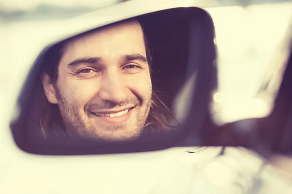 Happy young man driver looking in car side view mirror