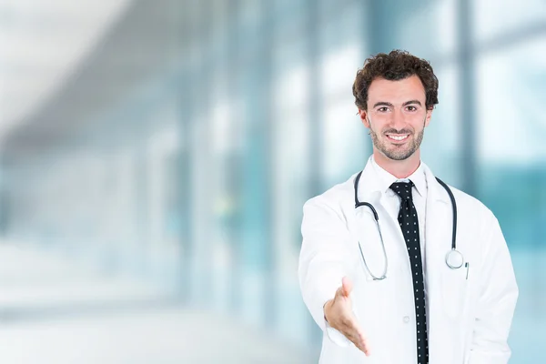 Doctor giving handshake smiling standing in hospital hallway
