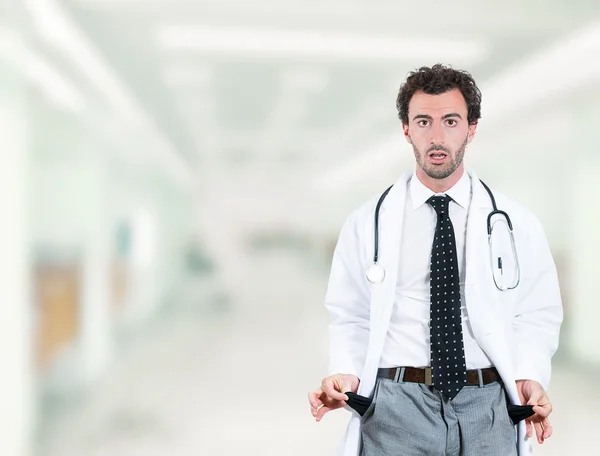 Doctor penniless showing empty pockets standing in hospital hallway