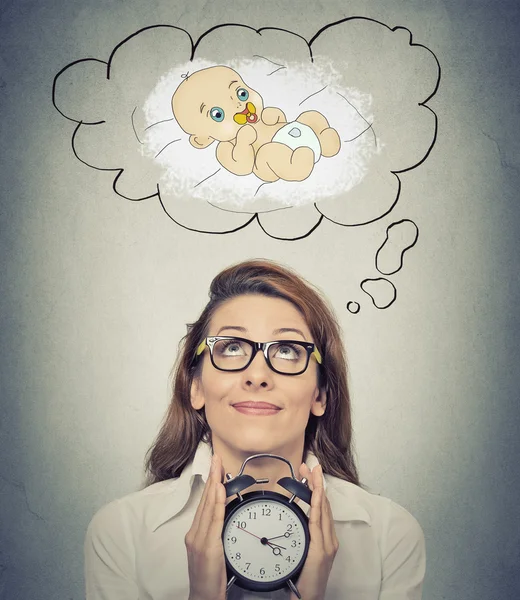 Woman anticipating a baby looking up holding alarm clock