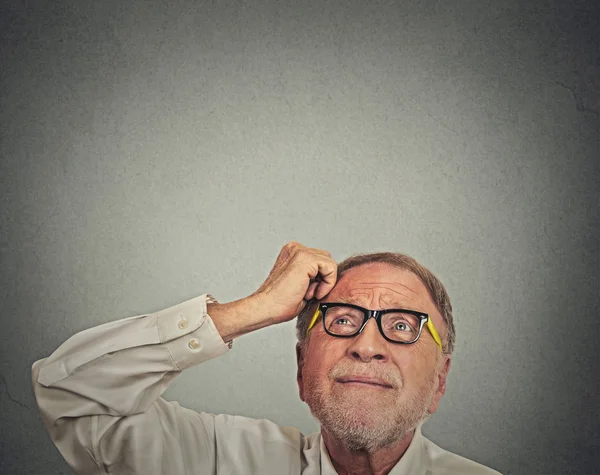 Undecided man with glasses scratching head thinking looking up