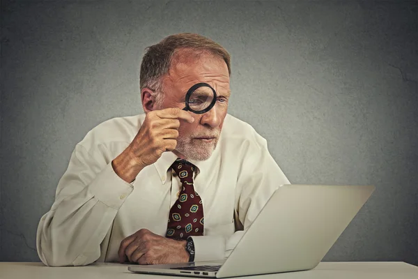 Man working on computer looking through magnifying glass at screen