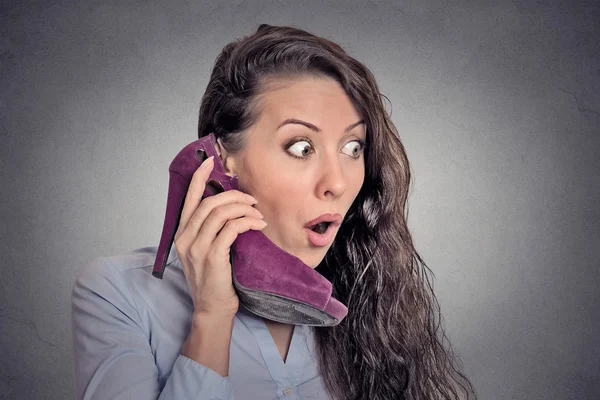 Surprised woman holding high heeled shoe in hand as phone