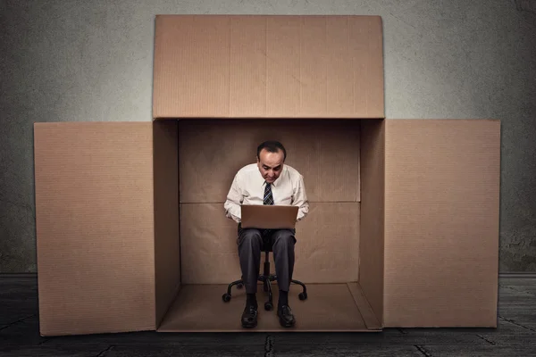 Man working on laptop sitting on chair inside carton box