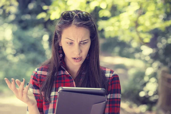 Skeptical unhappy serious woman using mobile pad computer outdoors