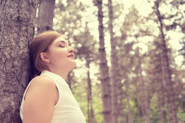 Relaxing young woman enjoying summer day in forest taking deep breath