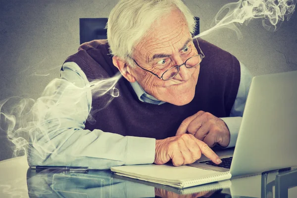 Frustrated elderly old man using laptop computer sitting at table