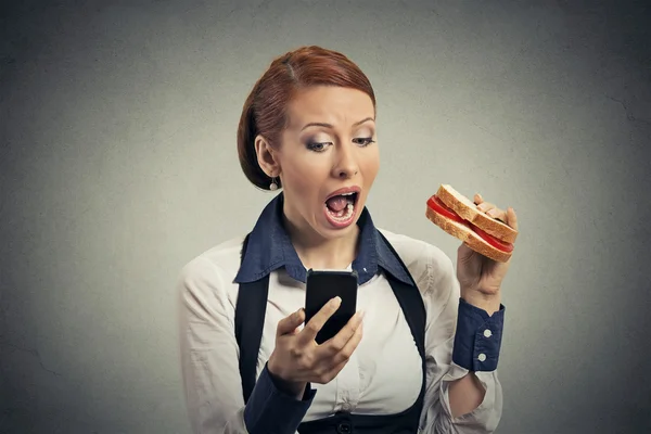 Business woman reading news on smart phone eating sandwich