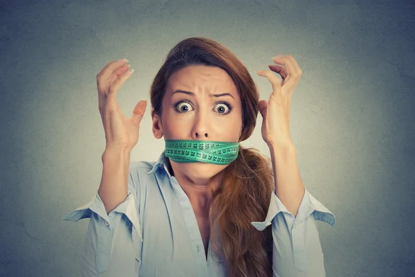 Frustrated woman with green measuring tape around her mouth