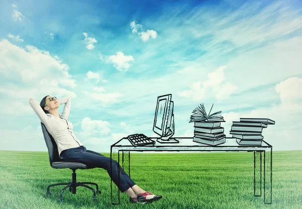 Businesswoman relaxing at her desk in the middle of a green meadow