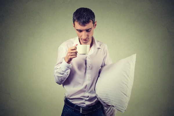 Very tired, almost falling asleep business man holding a cup of coffee and pillow