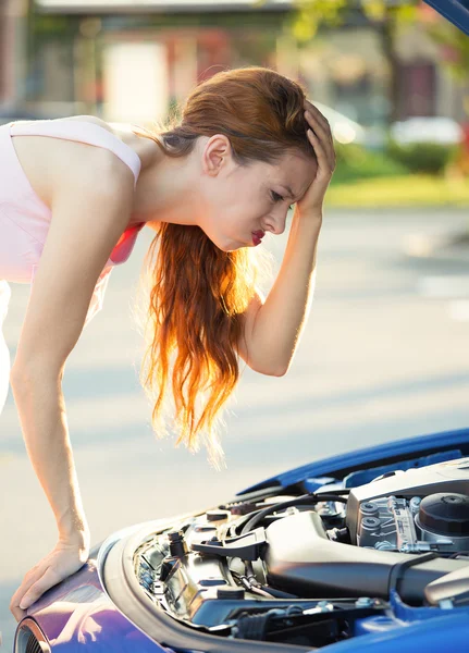 Stressed, angry young woman in front of her broken down car