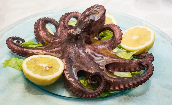 A boiled octopus, among lemons cut, on a glass dish, over a bed