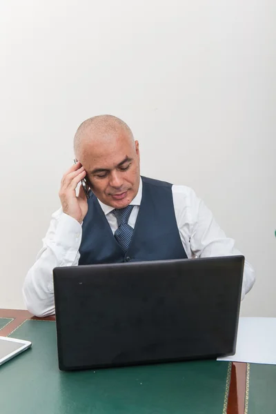 A business man on the phone and pc, at desk, in conference call