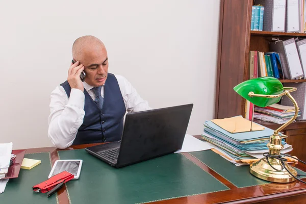 A business man on the phone and pc, at desk, in conference call