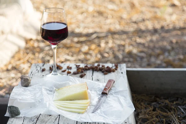 Pieces of cheese and raisins with a red wine glass on a old wood board
