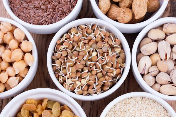 Bowls of various legumes and seeds. Lentils, sesame seeds, pistachio nuts, flaxseed, raisins, peanuts, chickpeas.