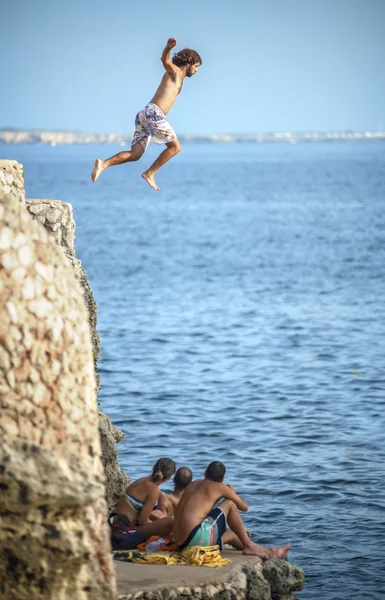 Menorca, Spain - September 8: Young man jumping from cliff into