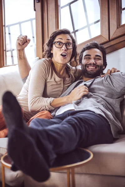 Young couple cheering for a sport team watching sports on TV