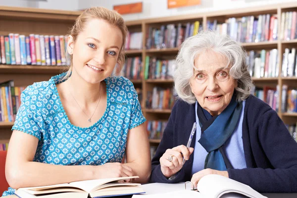 Senior Woman Working With Teacher In Library