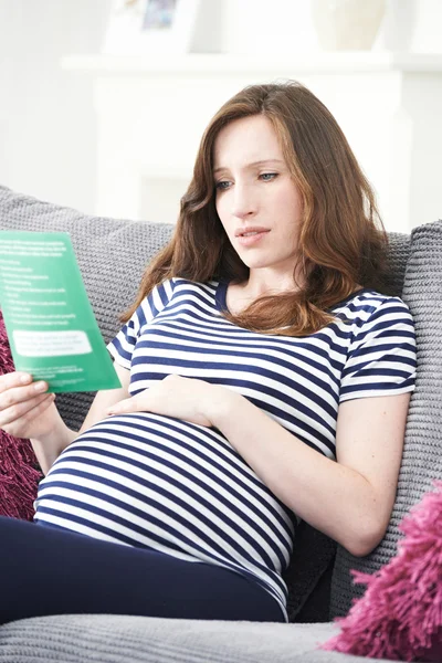 Concerned Pregnant Woman Reading Leaflet With Medical Advice