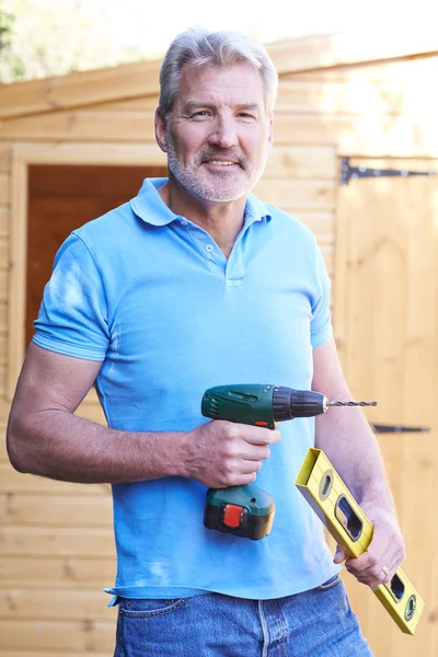 Handyman Standing Outside Garden Shed With Tools