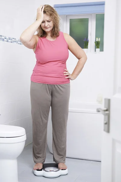 Overweight Woman Weighing Herself On Scales In Bathroom