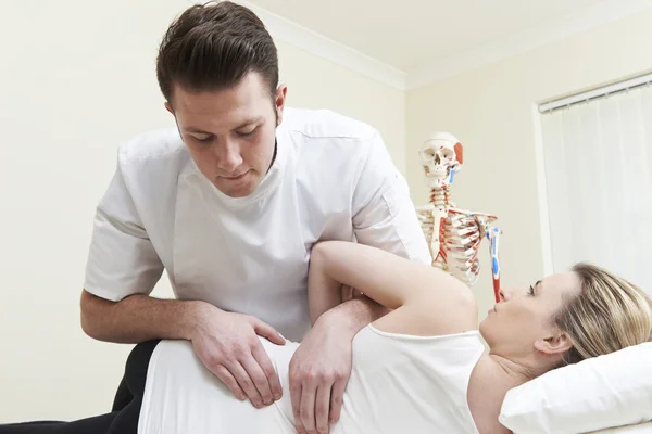 Male Osteopath Treating Female Patient With Back Problem