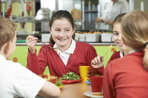 Group Of Pupils Sitting At Table In School Cafeteria Eating Lunc