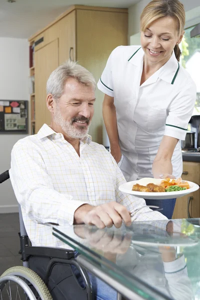 Carer Serving Meal To Man In Wheelchair At Home