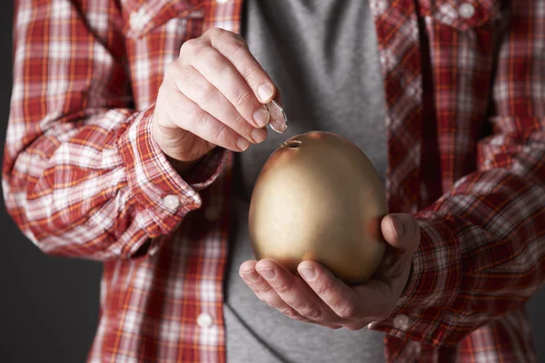 Man Putting Money Into Golden Egg Shaped Money Box