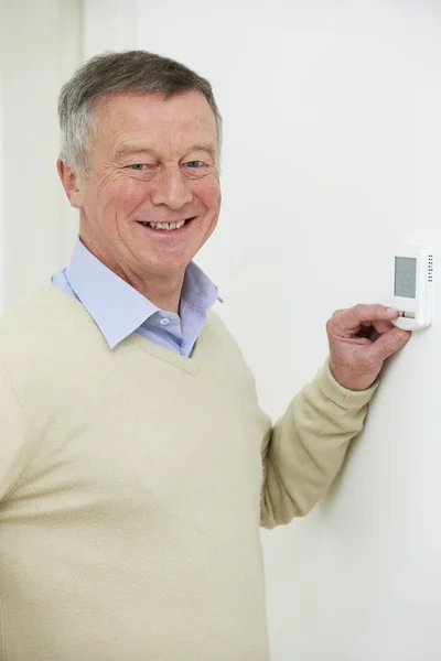 Smiling Senior Man Adjusting Central Heating Thermostat